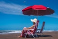 Mature woman relaxing on the beach sitting on a deckchair under an umbrella. Royalty Free Stock Photo