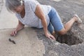 Mature woman or senior walking in a building zone and falling in a big hole with her leg inside it - needing help on the ground