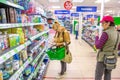 A mature woman with a shopping cart stands near a shelf with cleaning products in a store. Russian text: stationery, cosmetics, ho Royalty Free Stock Photo
