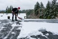 Mature woman shoveling fresh wet snow off a flat carport roof