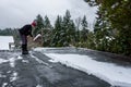 Mature woman shoveling fresh wet snow off a flat carport roof