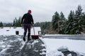 Mature woman shoveling fresh wet snow off a flat carport roof