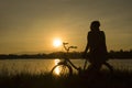 Mature woman sit at retro vintage bicycle near the lake at sunset moment. silhouette bicycle at the sunset with grass field. Royalty Free Stock Photo