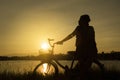 Mature woman sit at retro vintage bicycle near the lake at sunset moment. silhouette bicycle at the sunset with grass field. Royalty Free Stock Photo