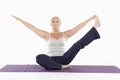 Mature woman sitting on mat and doing yoga with arms outstretched Royalty Free Stock Photo