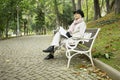 Mature woman sitting on a park bench think and reading a book. Royalty Free Stock Photo