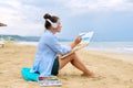 Mature woman sitting on sandy beach drawing sketch of sea