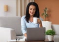 Mature woman sitting on sofa drinking coffe working on computer Royalty Free Stock Photo