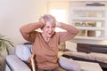 Mature woman sitting on a white sofa in a home touching her head with her hands while having a headache pain and feeling unwell Royalty Free Stock Photo