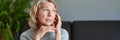 Mature woman sitting on a white sofa in a home touching her head with her hands Royalty Free Stock Photo