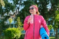 Mature woman in sports windbreaker with yoga mat bottle of water, walking outdoor Royalty Free Stock Photo