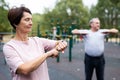 Mature woman in sportswear looks at fitness watch or at pedometer while exercising in city park