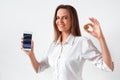 Cryptocurrency. Woman standing on white showing screen of smartphone with statistics holding coin smiling happy