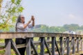 Mature woman standing on a wooden bridge taking photos with her cell phone Royalty Free Stock Photo