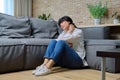 Mature woman suffering from neck pain, sitting on floor in living room Royalty Free Stock Photo