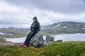 Mature woman takes pause and rests on stone, looking at her mobile, hiking high in Norwegian mountains. Healthy lifestyle. Norway