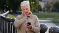 Mature woman texting messaging on modern smartphone gadget, gets read unexpected news, surprised, grandmother browse