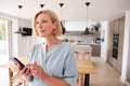 Mature Woman Using App On Mobile Phone To Control Central Heating Temperature In House Royalty Free Stock Photo