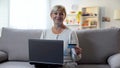 Mature woman using laptop, holding credit card and smiling at camera, banking Royalty Free Stock Photo