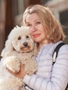 Mature woman walking with fluffy white dog in summer city