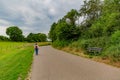 Mature woman walking with her dog on a paved path surrounded by farmland, trees and greenery with green foliage Royalty Free Stock Photo