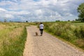 Mature woman walking with her short haired brown dachshund, back to camera, hiking trail Royalty Free Stock Photo