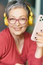 Mature woman wearing glasses, smiling and holding phone headphones on. Image portrays technology, communication, and