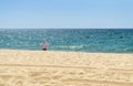 Mature woman in white shirt and white hat is standing on the beach and watching the sea.