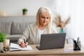 Mature woman writing and using pc laptop at home Royalty Free Stock Photo