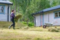 Mature women carrying fresh cut grass to garden wheelbarrow - summer gardening work at summer cottage. Side photo Royalty Free Stock Photo