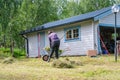 Mature women collecting fresh cut grass to garden wheelbarrow - summer gardening work at summer cottage. Rear photo Royalty Free Stock Photo