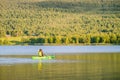 Mature women in green safety life jacket kayaking in green kayak. Rear long distance photo on still water