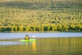 Mature women in green safety life jacket kayaking in green kayak. Rear long distance photo on still water