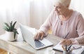 Mature working lady making notes, using laptop at home