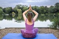 Mature yoga teacher relaxes and meditates by doing a pose beside a tranquil lake