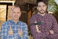 Mature and young men posing near wood hut holding axe Royalty Free Stock Photo