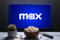 Max or HBO Max logo on TV with popcorn bowl, reomote control and home plant. Astana, Kazakhstan - July 21, 2023.