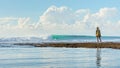 May 5 2019 : Balangan Beach, Bali, Indonesia - A woman watching as a surfer rides a nice wave with afternoon sun lighting the