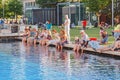 Crowd of people relaxing on the green grass and cooling their feet in a cool pond in hot weather Royalty Free Stock Photo