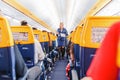 Interior of Ryaniar airplane with passengers on seats and stewardess in uniform walking the aisle