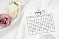 May 2025 calendar page and rose flower on white satin textile Royalty Free Stock Photo