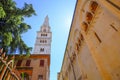 May 2022 Modena, Italy: Tower Ghirlandina and the facade of the Duomo Modena across the blue sky from beneath on the square piazza