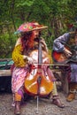 Muskogee USA Woman in gypsy costume with mustache plays Cello seated on bench in front of trees