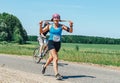 May 26-27, 2018 Naliboki,Belarus All-Belarusian amateur marathon Naliboki A woman runs alongside a cyclist on the road