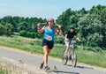 May 26-27, 2018 Naliboki,Belarus All-Belarusian amateur marathon Naliboki A woman runs alongside a cyclist on the road