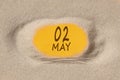 May 2. 2th day of the month, calendar date. Hole in sand. Yellow background is visible through hole