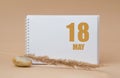 may 18. 18th day of the month, calendar date. White blank sheet of notepad, stones, dry sprig of grass, on beige