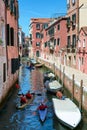 Tourists rowing in canoes doing a kayak tour in Venice, surrounded by beautiful view of picturesque old buildings