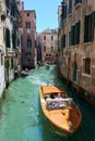 View of narrow canal in Venice, Italy, with boat and gondolas surrounded by picturesque old buildings Royalty Free Stock Photo