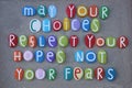 May your choices reflect your hopes, not your fears, life quote composed with multi colored stone letters over beach sand